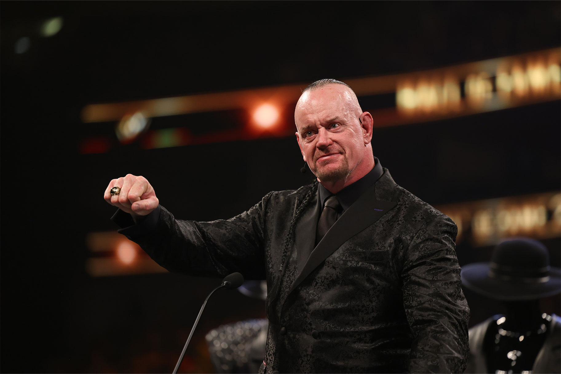 The Undertaker dressed in all black, with a smile on his face, in the the WWE ring