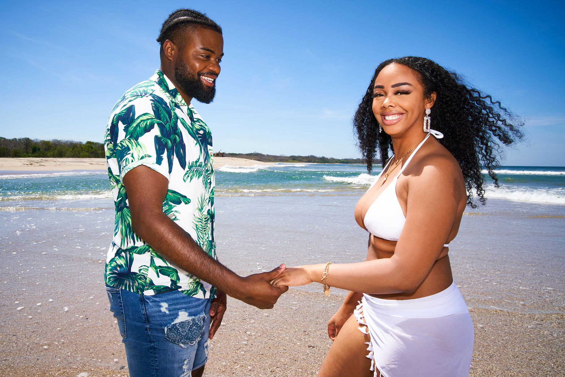 The Big D's Devon and Alexis walk along the beach while smiling at the camera