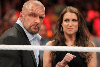 Stephanie McMahon standing behind Triple H, looking at him