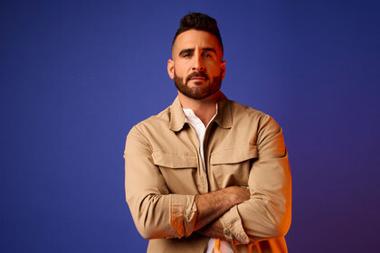 Paul Swan standing in front of a blue backdrop with a serious look on his face