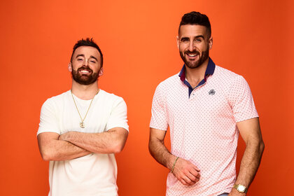 Austin and Paul standing in front of an orange backdrop