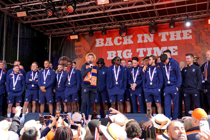 Luton Town manager Rob Edwards speaks to fans while the team stands behind him