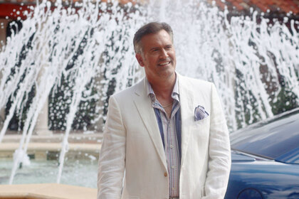 Bruce Campbell as Sam Axe, standing in front of a water fountain