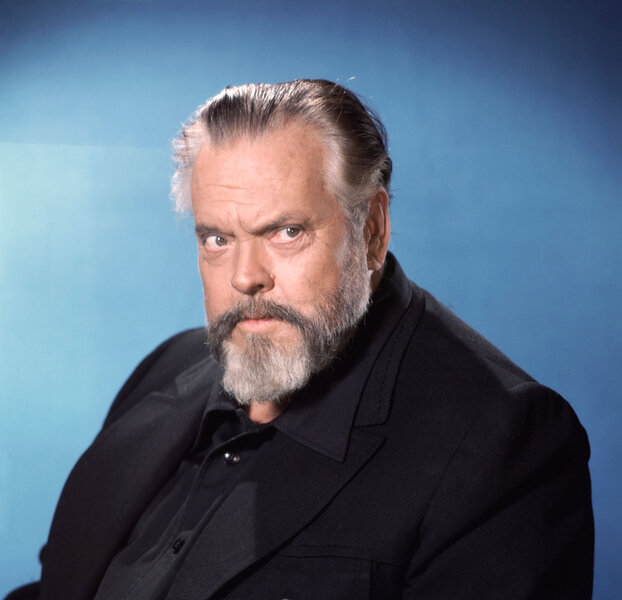 Orson Welles wearing a black blazer in front of a blue background