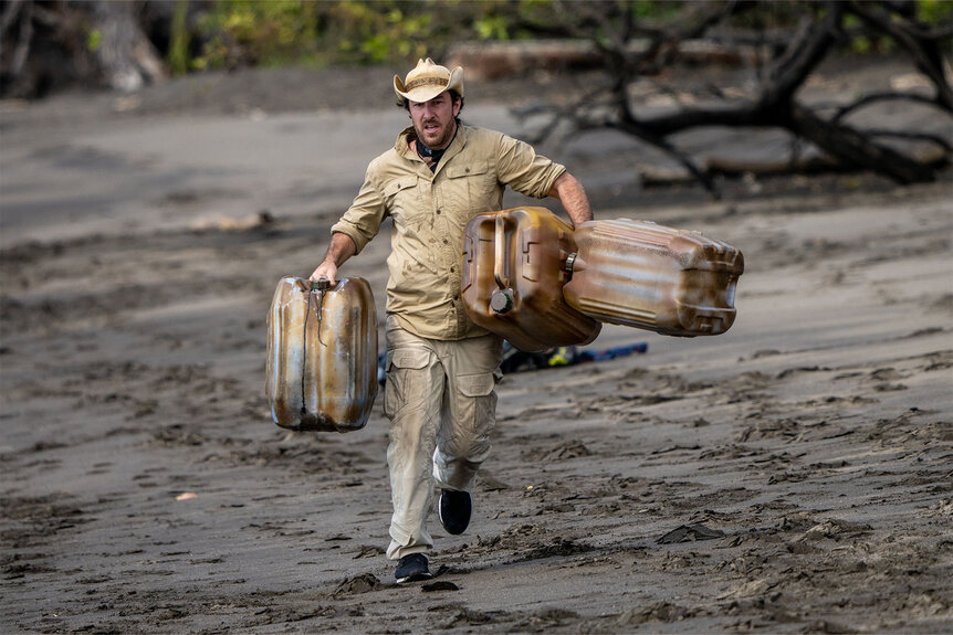 Snake In The Grass Contestant running while holding three large water jugs