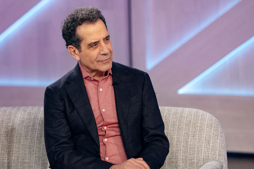 Tony Shalhoub sits on a couch on the set of The Kelly Clarkson Show