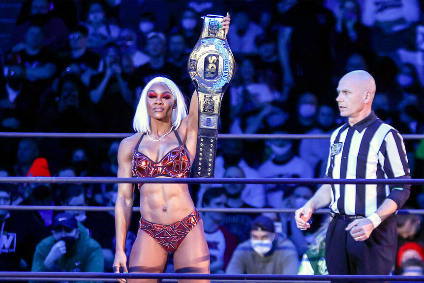 Jade Cargill holds her belt above her head while standing in the center of the ring