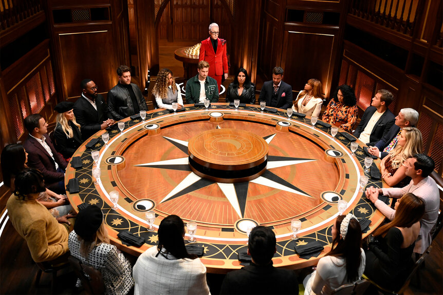 Alan Cumming stands at a table with the contestants of The Traitors Season 2