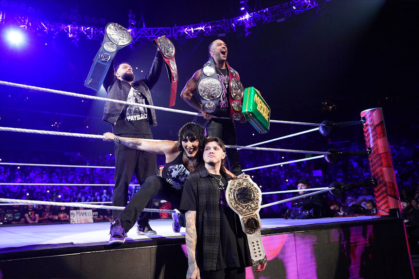 Rhea Ripley and Dominik Mysterio pose outside of the ring with Roman Reigns and Damian Priest