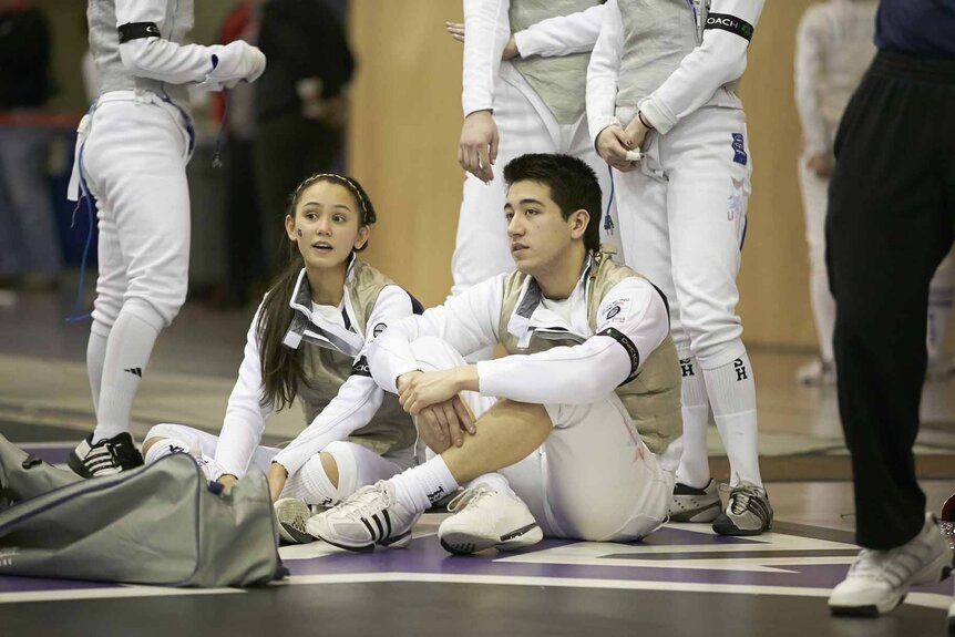 Gerek Meinhardt and Lee Kiefer sit together on the floor in fencing gear.