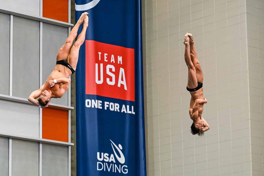 Gregory Duncan and Tyler Downs dive past a Team USA banner.