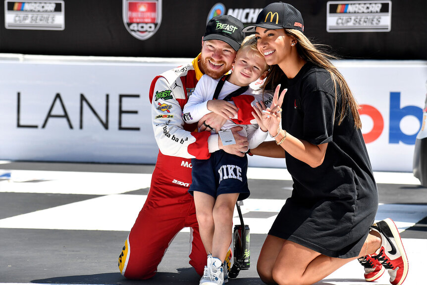 Tyler Reddick embraces his wife, Alexa De Leon and son Beau Reddick in victory lane after winning the NASCAR Cup Series FireKeepers Casino 400